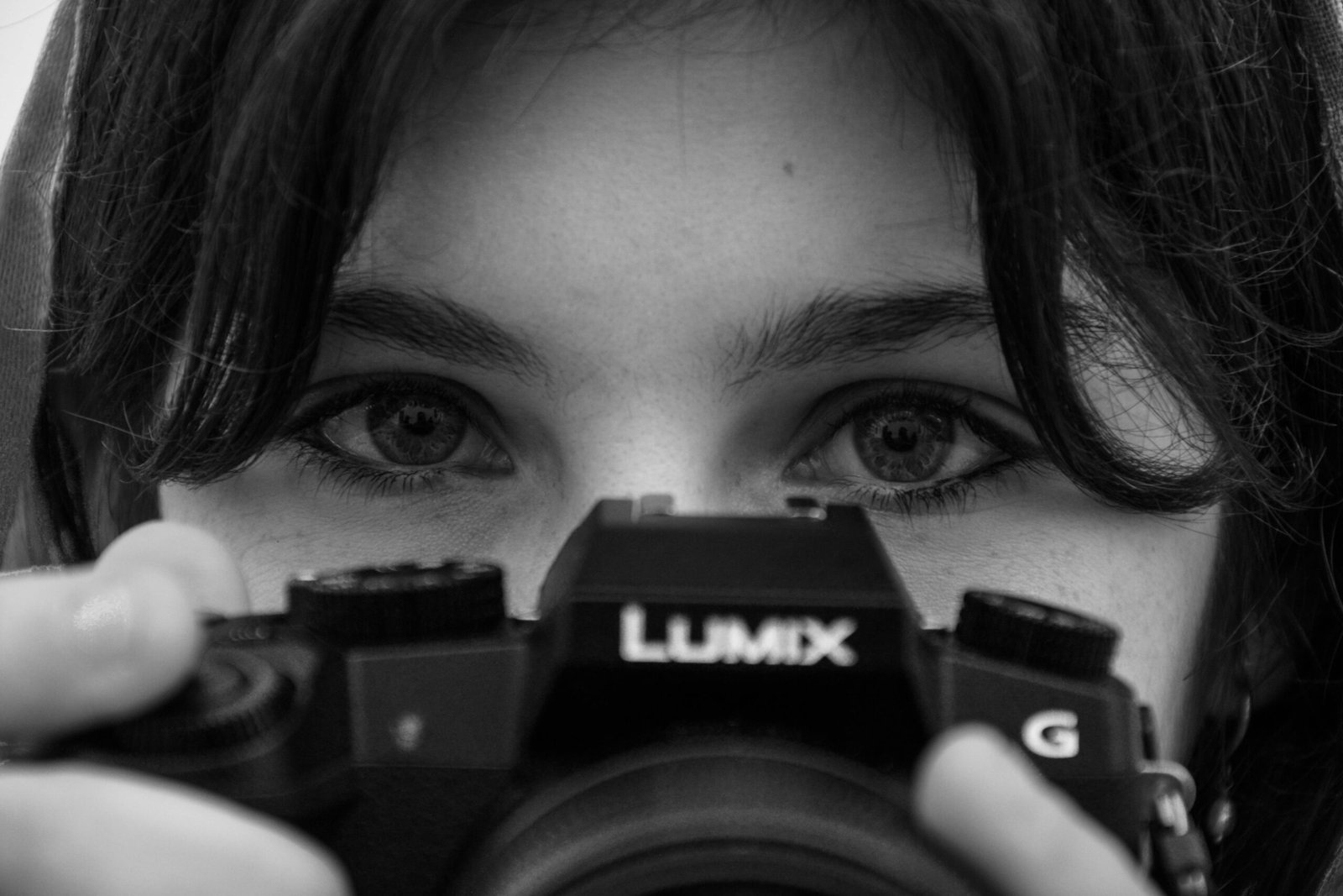 Black and white photo of a person holding a camera with intense focus on their eyes.