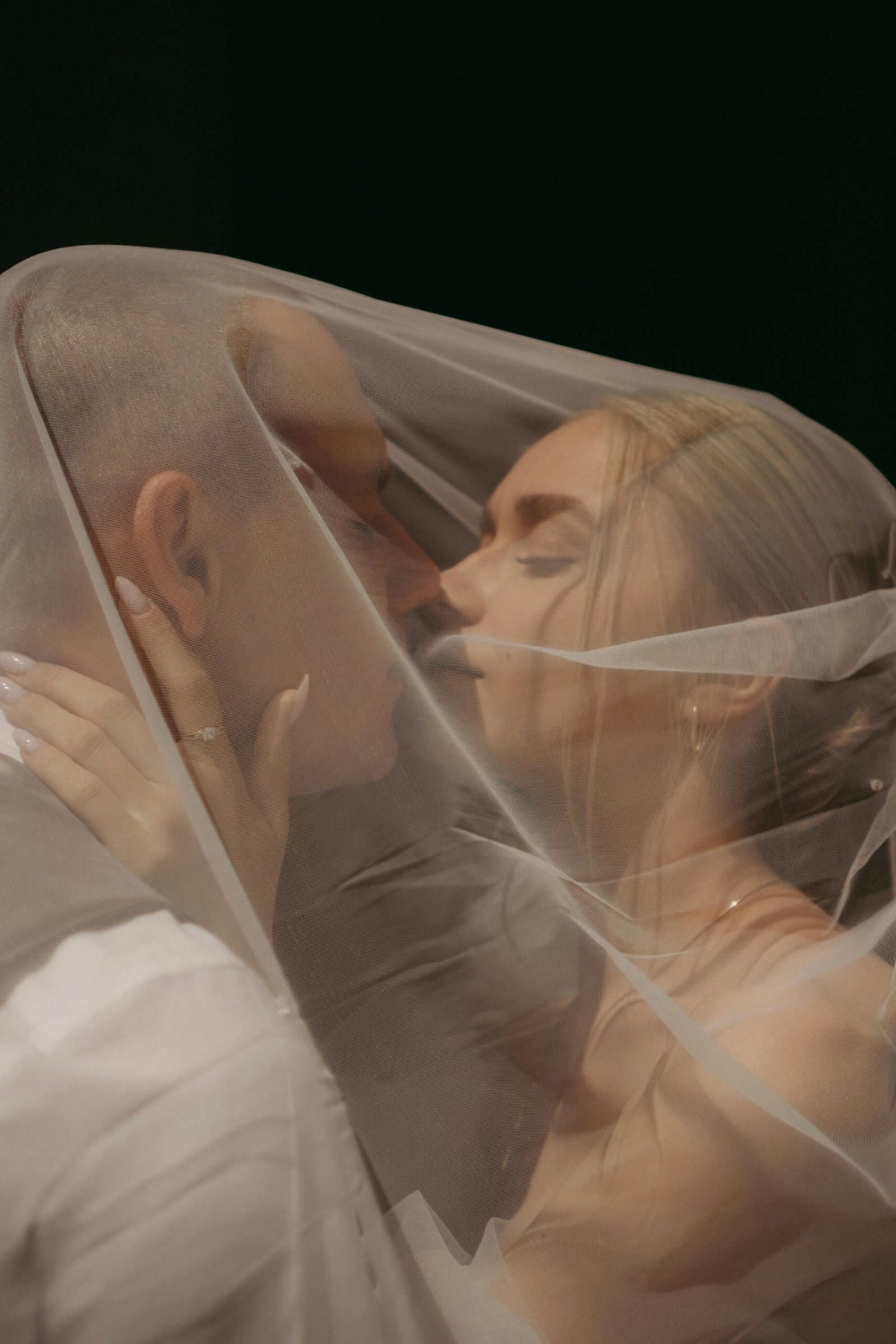 Close-up of a kissing couple wrapped in a wedding veil, capturing an intimate moment.